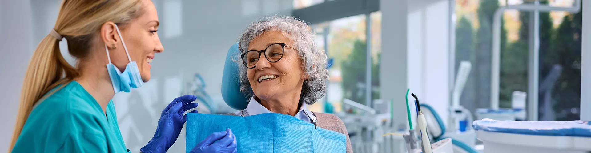 Smiling elderly woman interacting with a friendly dentist in a bright, modern dental clinic.