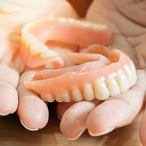 Close-up of a person holding a set of dentures, highlighting removable dental prosthetics for missing teeth.