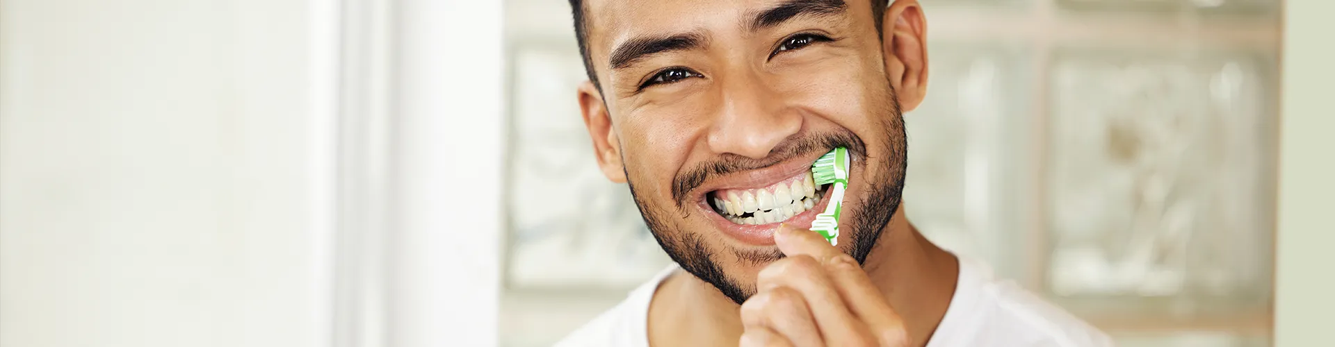 Smiling man brushing his teeth with a green toothbrush, emphasizing good oral hygiene and daily dental care.