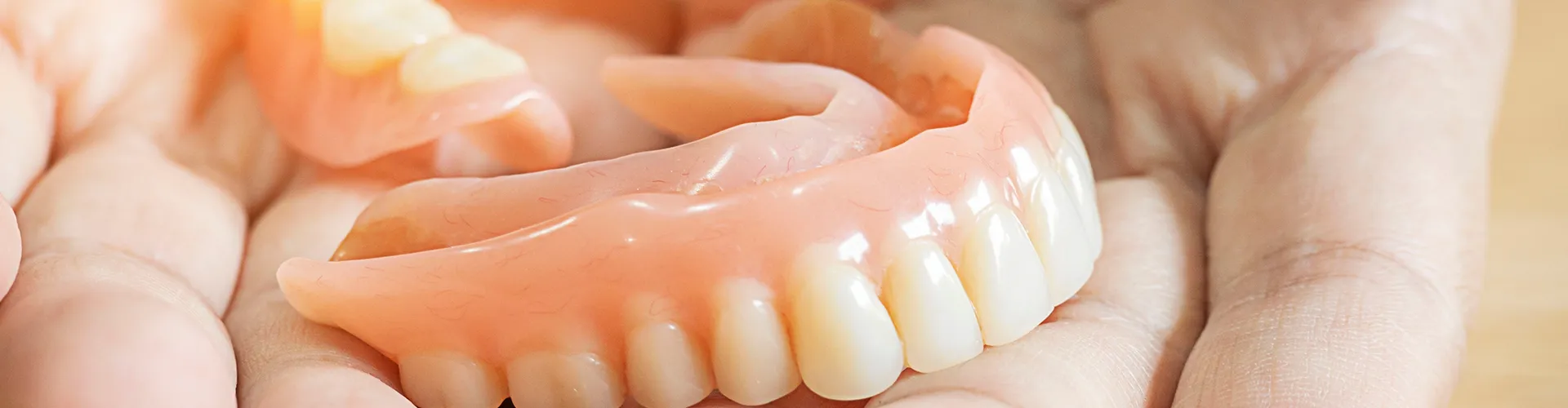 Close-up of a person holding a set of dentures, highlighting removable dental prosthetics for missing teeth.